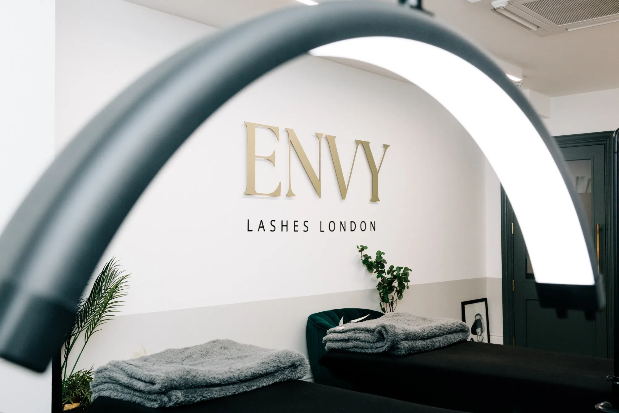 The gold ENVY Lashes London sign seen through a lash lamp, above the treatment beds